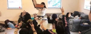 An image of a group of teens holding up their hands making "peace" signs, with one person holding up a box of pizza
