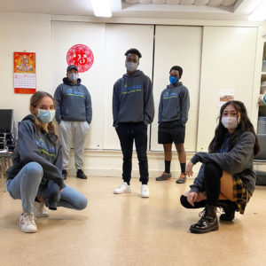 An image of five teens wearing masks, and standing apart from each other, facing the viewer