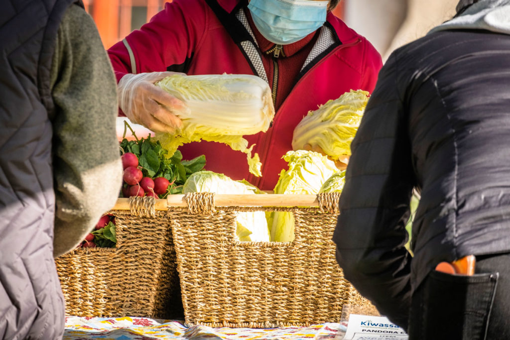 A volunteer hands cabbage from a basket to market-goers