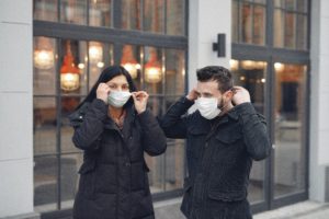 An image of two people outdoors, putting on masks before entering a building
